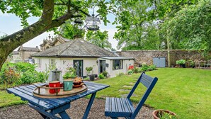 Ein rustikales Haus mit Mauerwerk, ein Garten mit Rasen und ein Tisch mit Gartenmöbeln.