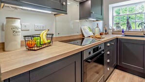 Eine moderne Küche mit dunklen Schränken, einer Holz Arbeitsplatte, einem eingebauten Ofen und einem Fenster mit Blick ins Grüne.