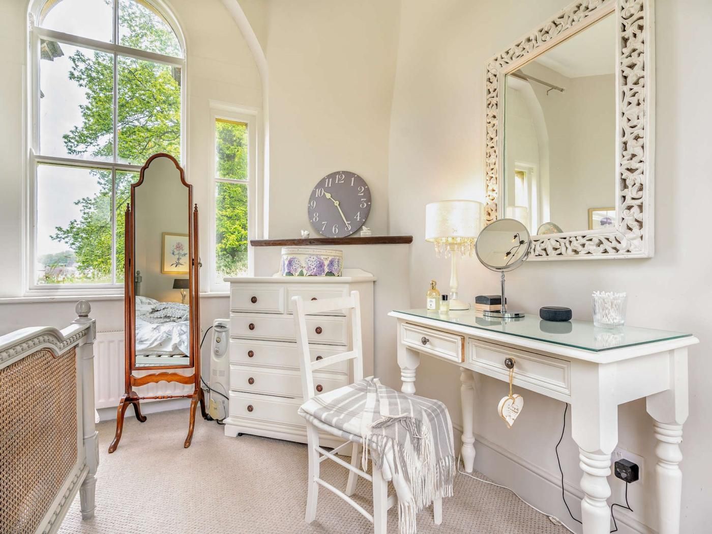 A bedroom with a large mirror, a dresser, a chair, and a clock.