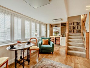 A room with a dining table, a green armchair, a staircase, and a bookshelf. - 1 Bed in Ilminster (oc-78353) (Ilminster)