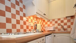 A compact kitchen with a checkered backsplash, a built-in oven, a dishwasher, and a sink. - 1 Bed in Sturminster Newton (oc-29117) (Hazelbury Bryan)
