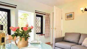 A dining area with a table set for two, a grey sofa, and a window with a view. - 1 Bed in Sturminster Newton (oc-29117) (Hazelbury Bryan)