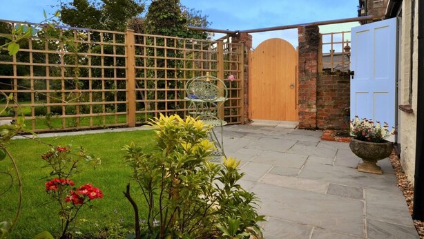 A garden with a wooden gate, a paved patio, and a brick wall. - 1 Bed in Sturminster Newton (oc-29117) (Hazelbury Bryan)
