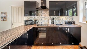 A modern kitchen with a wooden countertop, black cabinets, a tiled backsplash, and a large window. - 1 Bed in Fordingbridge (oc-49266) (Frogham)