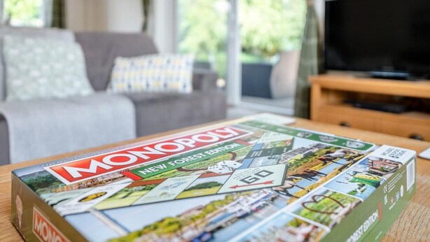A living room with a sofa, a coffee table with a Monopoly board game, and a television. - 1 Bed in Fordingbridge (oc-49266) (Frogham)