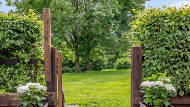 A wooden gate leading to a grassy area with a hedge on one side and a planter with white flowers on the other. - 2 Bed in Blandford Forum (oc-83013) (Woolland)