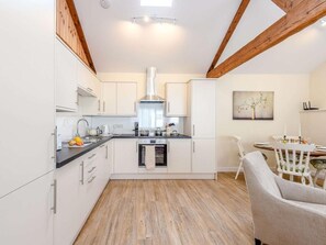 A compact kitchen with white cabinets, a central island, and a dining area with a white table and chairs. - 2 Bed in Blandford Forum (oc-83013) (Woolland)
