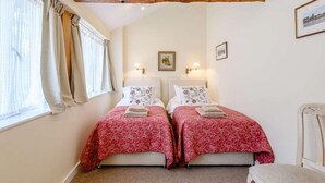 A bedroom with two beds, a wooden ceiling beam, a window with curtains, and two wall-mounted lamps. - 2 Bed in Blandford Forum (oc-83013) (Woolland)
