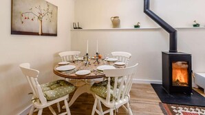 A dining area with a round table, white chairs, and a black wood-burning stove. - 2 Bed in Blandford Forum (oc-83013) (Woolland)