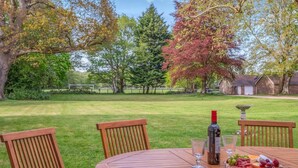 A wooden table with chairs in a backyard setting, a bottle of wine, glasses, and a cheese board with grapes. - 4 Bed in Lyndhurst (oc-nfl57) (Lyndhurst)