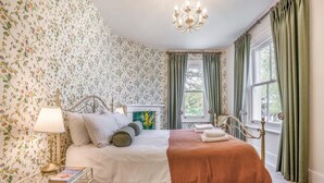 A bedroom with floral wallpaper, a bed with pillows, a bedside table with a lamp, and a window with curtains. - 4 Bed in Lyndhurst (oc-nfl57) (Lyndhurst)