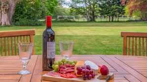 A picnic setup with a bottle, glasses, and a variety of food on a wooden table. - 4 Bed in Lyndhurst (oc-nfl57) (Lyndhurst)