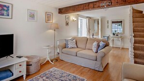 Un salon avec un canapé beige, une petite table blanche, un lampadaire et un meuble pour la télévision.
