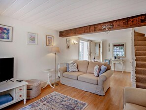 Ein Wohnzimmer mit einem beigen Sofa, einem kleinen weißen Tisch, einer Stehlampe und einem Fernsehschrank.