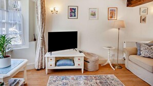 Un salon comprenant un téléviseur à écran plat, un canapé, une table basse, une lampe et une plante en pot.
