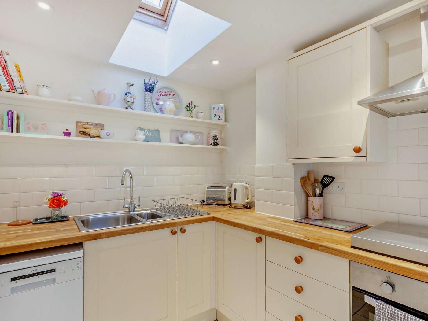 A compact kitchen with white cabinetry, a built-in dishwasher, a toaster, and a window above the sink.