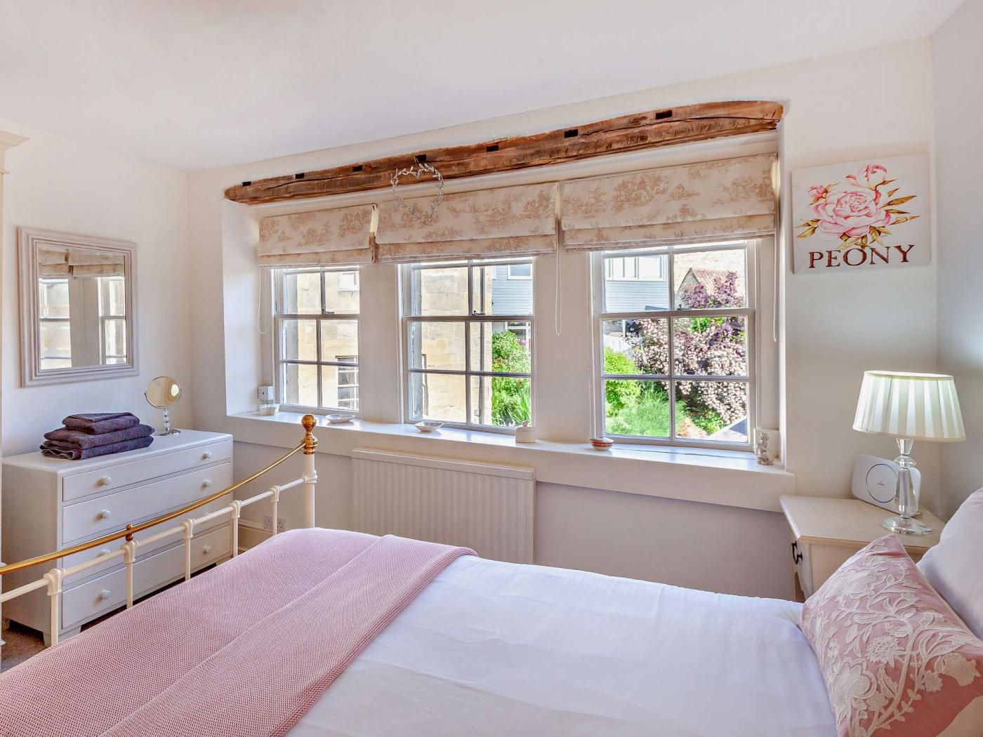 A bedroom with a bed, a dresser, a vanity with a mirror, and a window with a view of greenery.