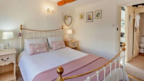 Une chambre à coucher comprenant un lit, des tables de chevet, une commode, un meuble à tiroirs, un miroir, un élément décoratif mural en forme de cœur et une porte donnant sur une autre pièce.