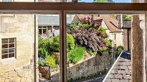 Un bâtiment en pierre avec une fenêtre, une rue étroite et un jardin où poussent différentes espèces de plantes.