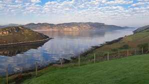 A coastal landscape with a calm body of water, grassy areas, and distant mountains.