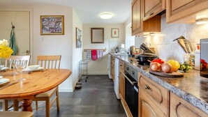 A kitchen with wooden cabinets, a dining table with chairs, a kitchen island, and various cooking utensils.