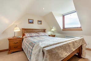 A bedroom with a sloped ceiling, a bed with a plaid bedspread, two bedside lamps, a nightstand with a lamp, and a window with a view.