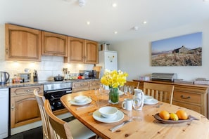 A modern kitchen with wooden cabinets, a dining table set for four, and a painting of a landscape on the wall.