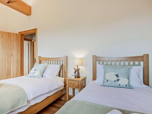 A bedroom with two wooden beds, a nightstand with a lamp, and a door leading to another room. - 2 Bed in Ulverston (oc-93091) (Osmotherley)