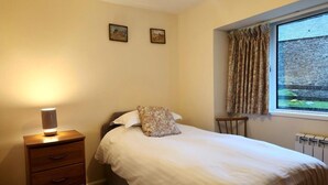 A bedroom with a bed, a bedside table with a lamp, a dresser, two wall-mounted pictures, a window with curtains, and a radiator. - 3 Bed in Kendal (oc-sz466) (Longsleddale)