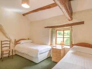 Un dormitorio con dos camas individuales, una silla de madera, una mesita de noche, un ventanal con vistas a la vegetación y vigas de madera a la vista en el techo.