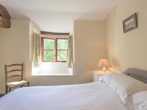 Une chambre à coucher avec un lit, une chaise, une table de chevet avec une lampe, une fenêtre avec des rideaux et un tableau encadré au mur.