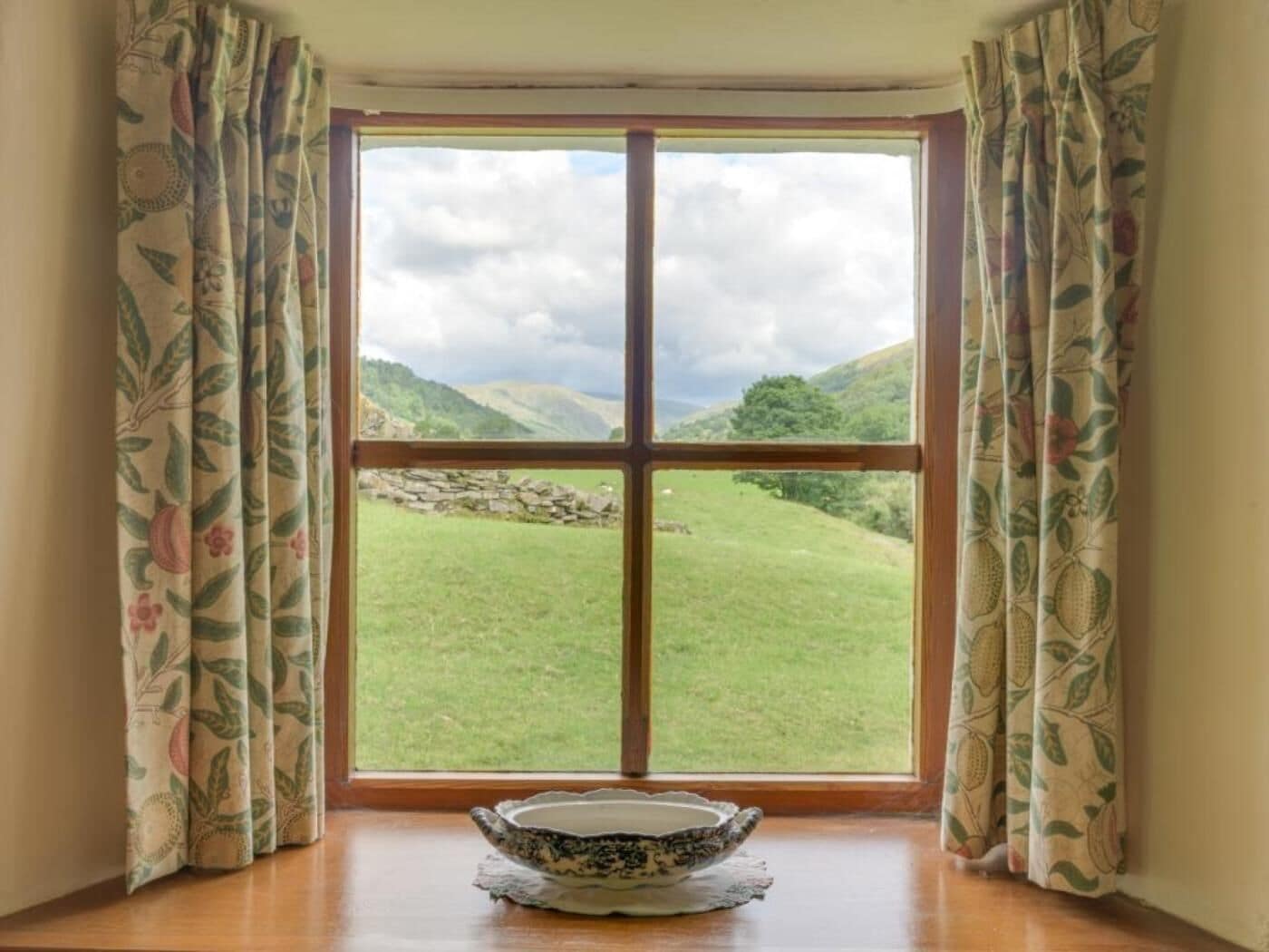 A room with a large window, a stone wall, and a bowl on the windowsill.