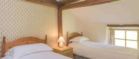 Une chambre avec deux lits simples, des poutres en bois, une fenêtre avec des rideaux et un papier peint à motifs.