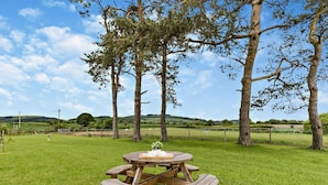 A picnic table in a grassy field with trees and a distant view of hills. - 1 Bed in Bucknell (oc-94661) (Letton)