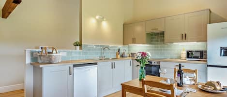 A modern kitchen with a central island, white cabinetry, and a wooden dining table with chairs.