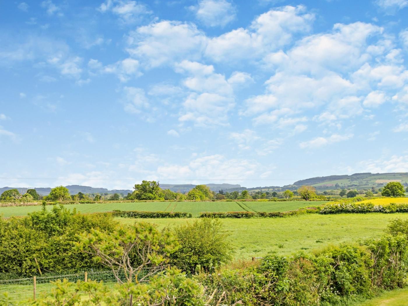 A rural landscape with rolling hills, a clear sky, and a fence in the foreground.