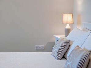 A neatly made bed with a white comforter and patterned pillows, a bedside lamp, and a white nightstand with a power outlet. - 1 Bed in Bucknell (oc-94662) (Letton)