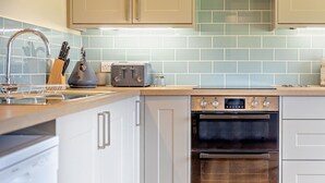 Uma cozinha moderna com armários brancos, fogão de aço inoxidável, forno embutido e backsplash com azulejos azul claro.
