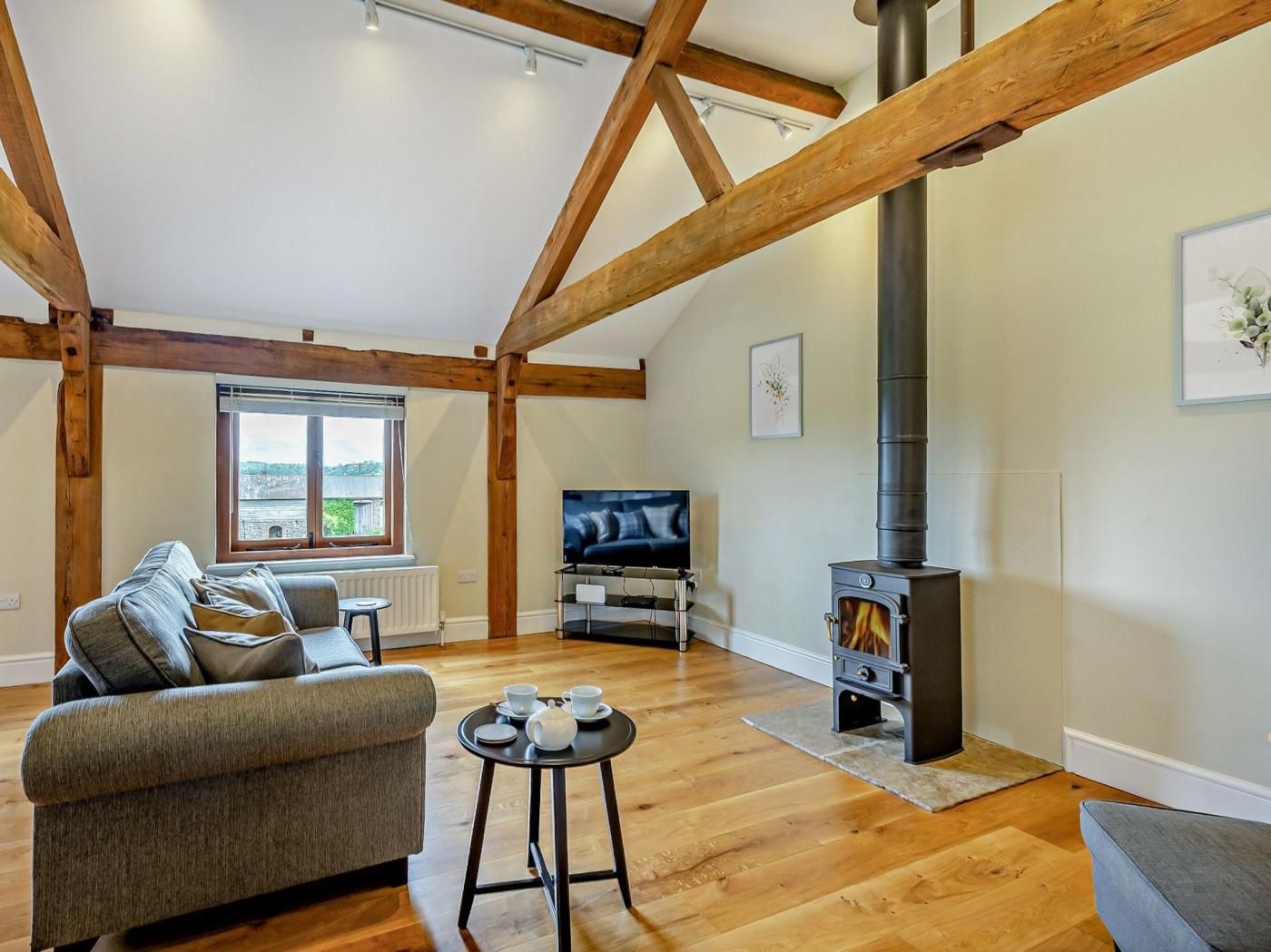 A loft-style living room with exposed wooden beams, a fireplace, a sofa, a television, and a window with a view.