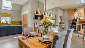 A dining area with a wooden table, chairs, and hanging pendant lights. - 2 Bed in Auchterarder (oc-94546) (Auchterarder)