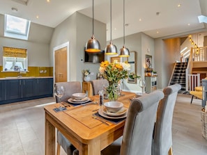 A dining area with a wooden table, chairs, and hanging pendant lights. - 2 Bed in Auchterarder (oc-94546) (Auchterarder)