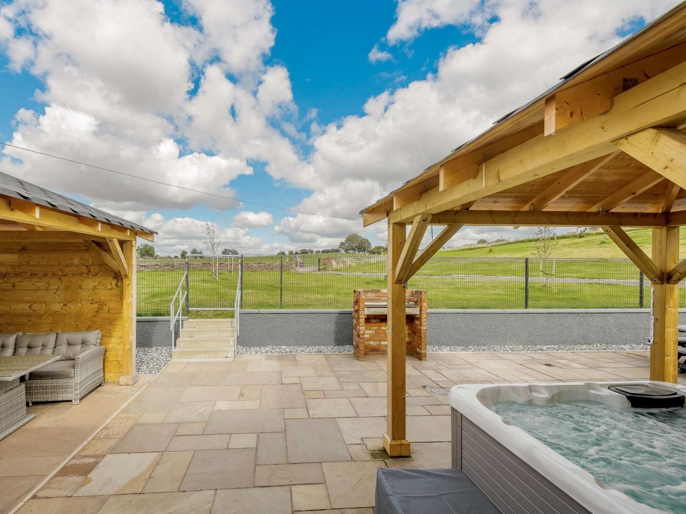 A covered outdoor area with a hot tub, seating, and a view of a grassy field.