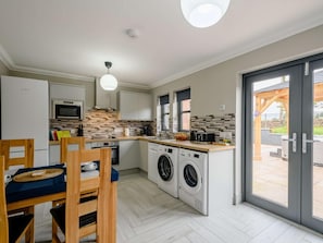 A compact kitchen with a built-in washing machine, a dining area with a table and chairs, and a sliding glass door leading to an outdoor area. - 3 Bed in Alexandria (oc-88753) (Balloch)