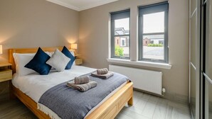 Une chambre avec un lit en bois, deux tables de chevet, une grande fenêtre et un radiateur.