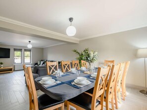 Un coin repas avec une table dressée pour quatre personnes, entouré de chaises en bois, d’un canapé et d’un téléviseur en arrière-plan.