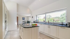 A modern kitchen with a central island, white cabinetry, a large window, and a view of greenery outside. - 8 Bed in Bridport (oc-53172) (South Poorton)