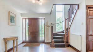A spacious hallway with a wooden floor, a staircase with a wooden railing, and a door leading outside. - 8 Bed in Bridport (oc-53172) (South Poorton)