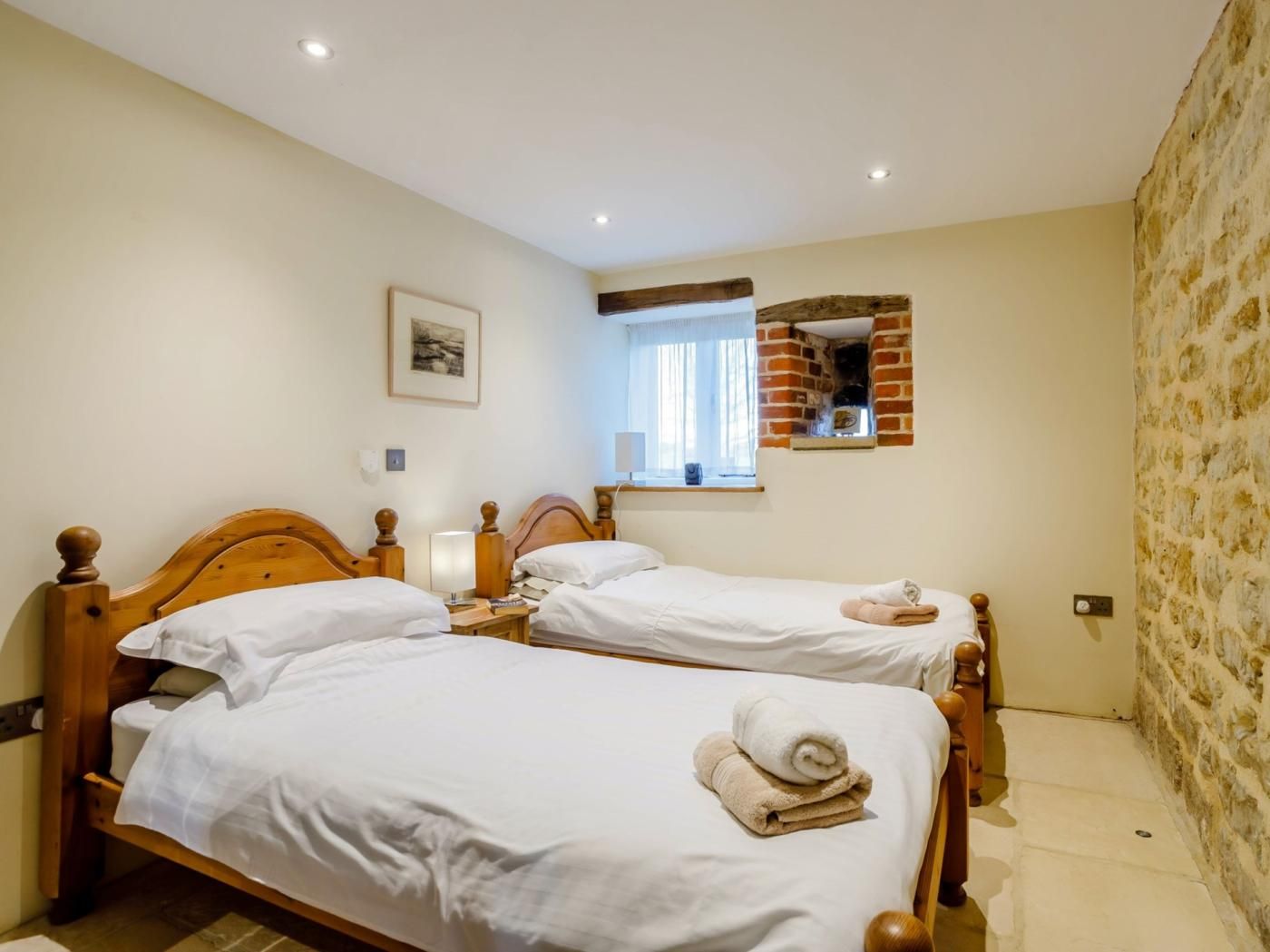 Une chambre d’hôtel avec deux lits en bois, une petite fenêtre donnant sur un paysage agréable et un mur en briques.