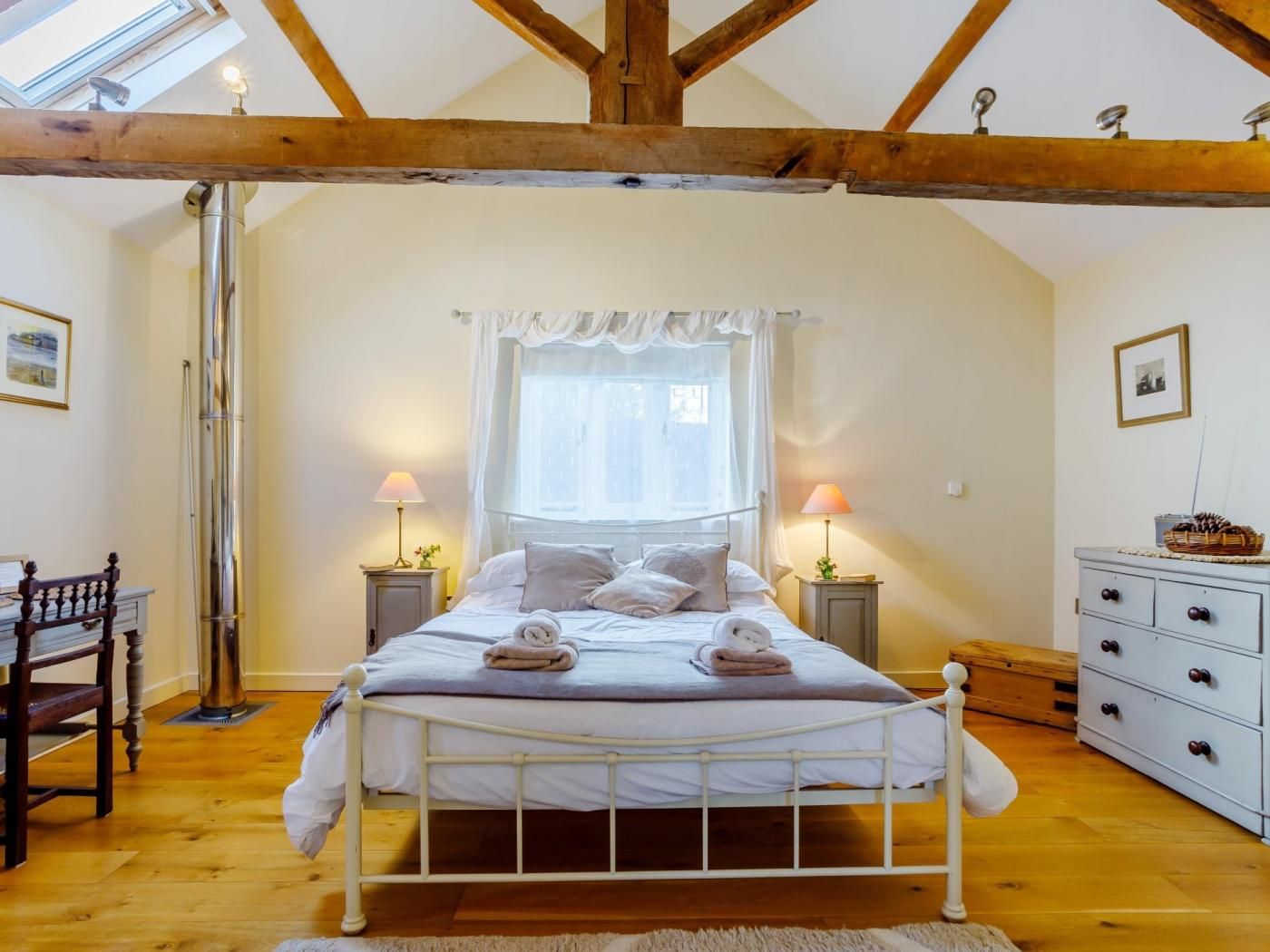 A bedroom with a bed, bedside lamps, a wooden dresser, a chair, and a skylight.