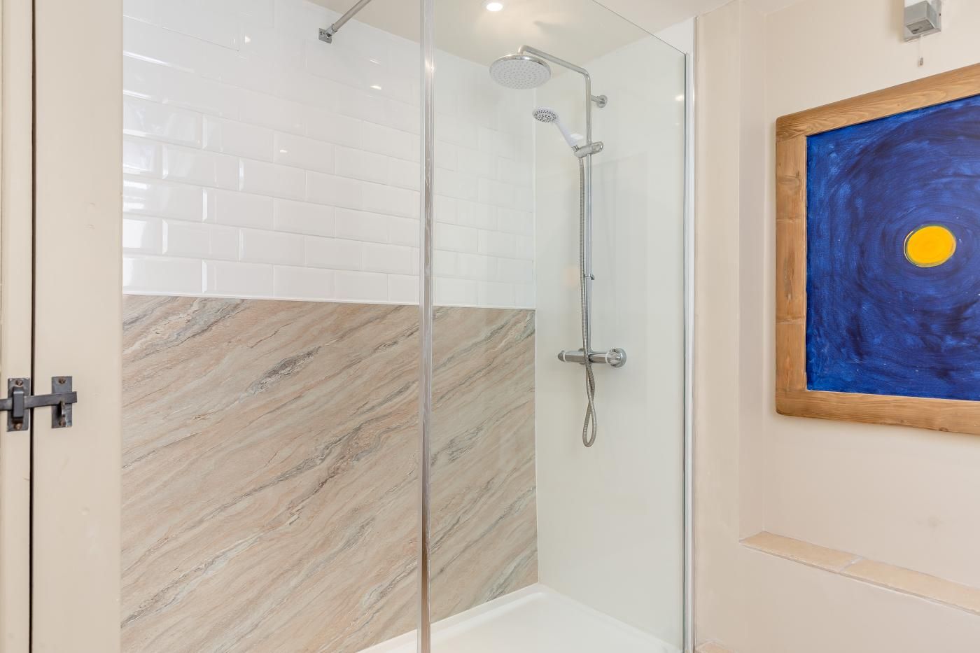 A shower with a glass door, a marble floor, and a painting on the wall.